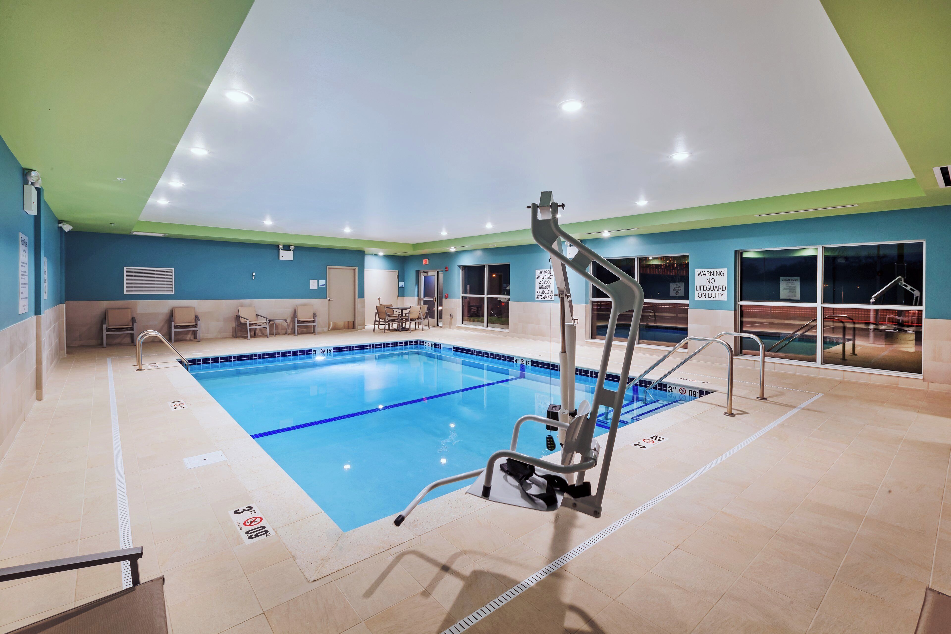 A swimming pool with safety railings, a ceiling with recessed lighting, and a blue and green wall color scheme.