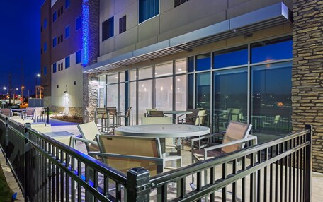 An outdoor patio area with round tables and chairs, a stone facade, and large windows.