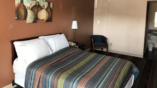 A hotel room with a bed, a chair, a lamp, and artwork on the wall. - Town Motel (Oshkosh)