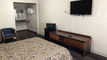 A hotel room with a bed, a wooden dresser, a television mounted on the wall, a chair, and a microwave on a small table.