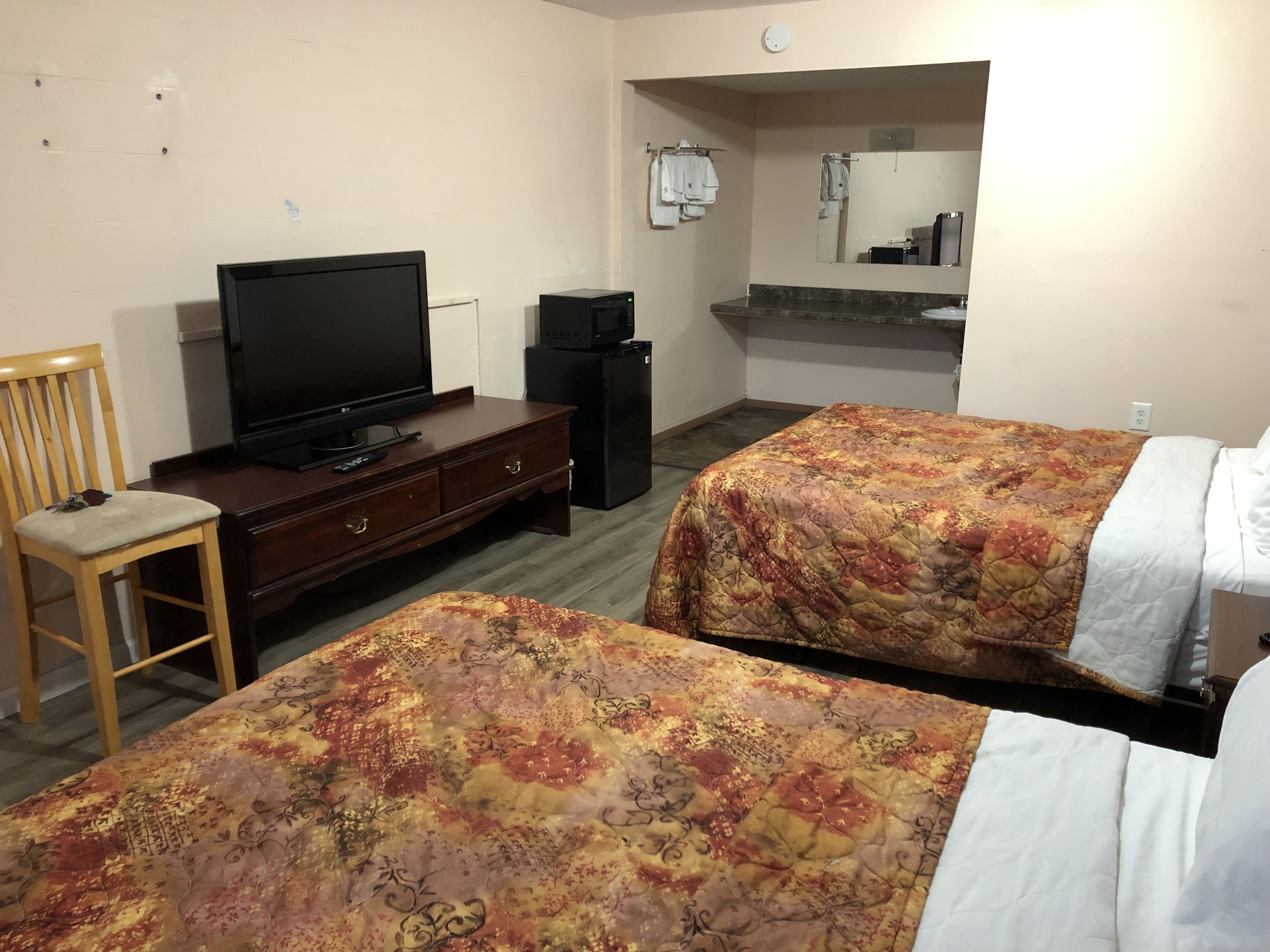 A hotel room with two beds, a TV, a dresser, and a mirror.