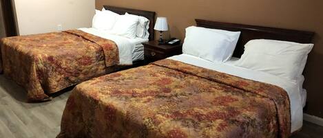Dos camas individuales con colchas florales a juego, una mesita de noche con lámpara y un enchufe de pared.