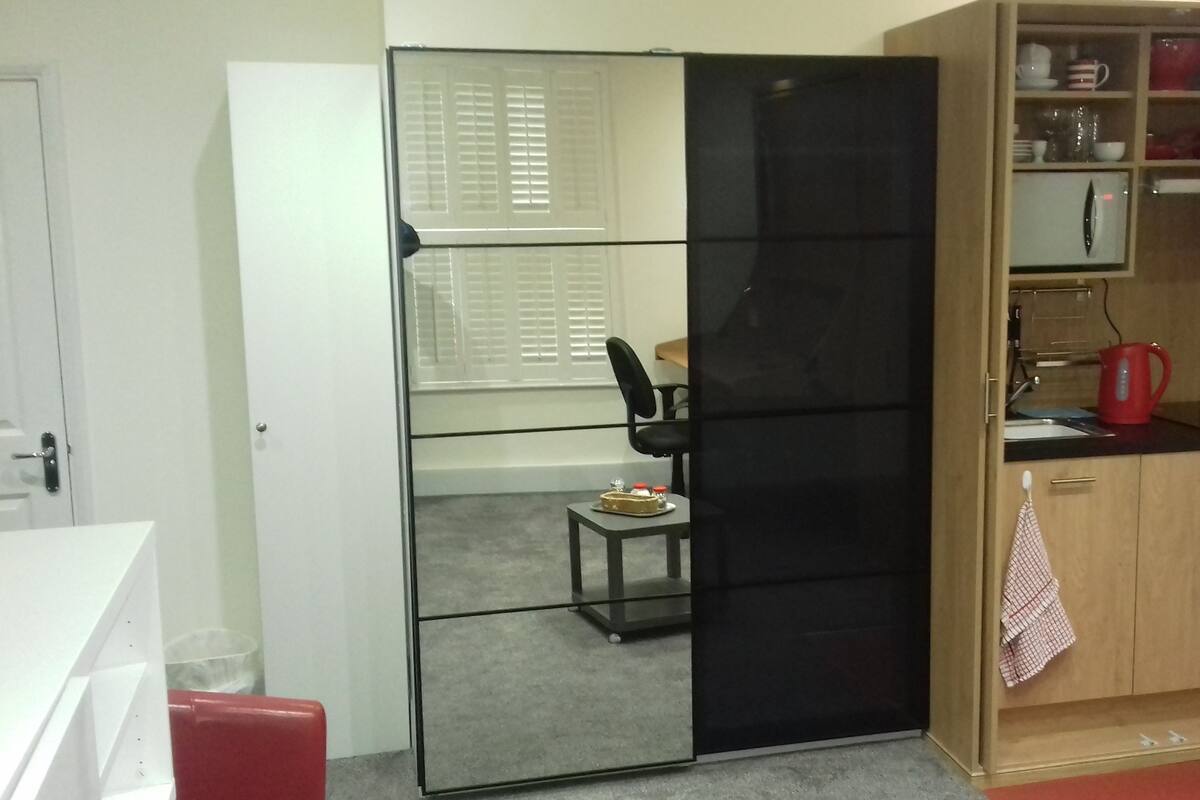 Eine kleine Küche mit schwarzem Kühlschrank, Holzschränken und einer Essecke mit Stuhl und Tisch.