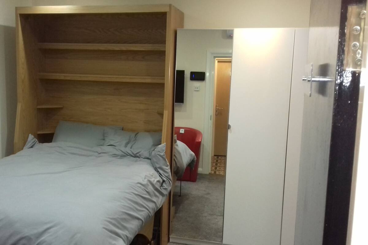 Ein Einzelbett mit Holz-Kopfstück, ein roter Sessel und ein Kleiderschrank.