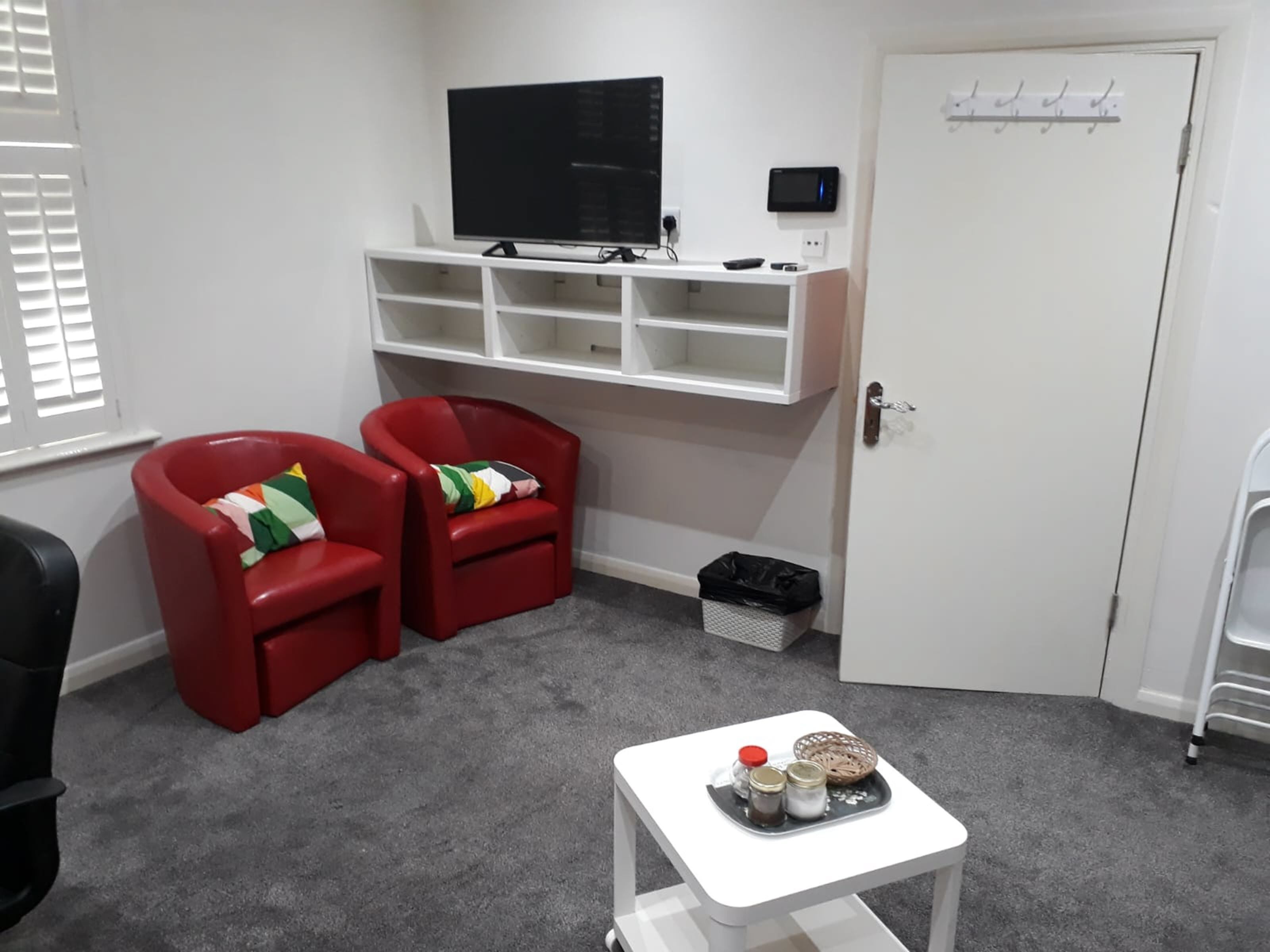 A room with two red chairs, a white table with jars, a TV, and a white door.