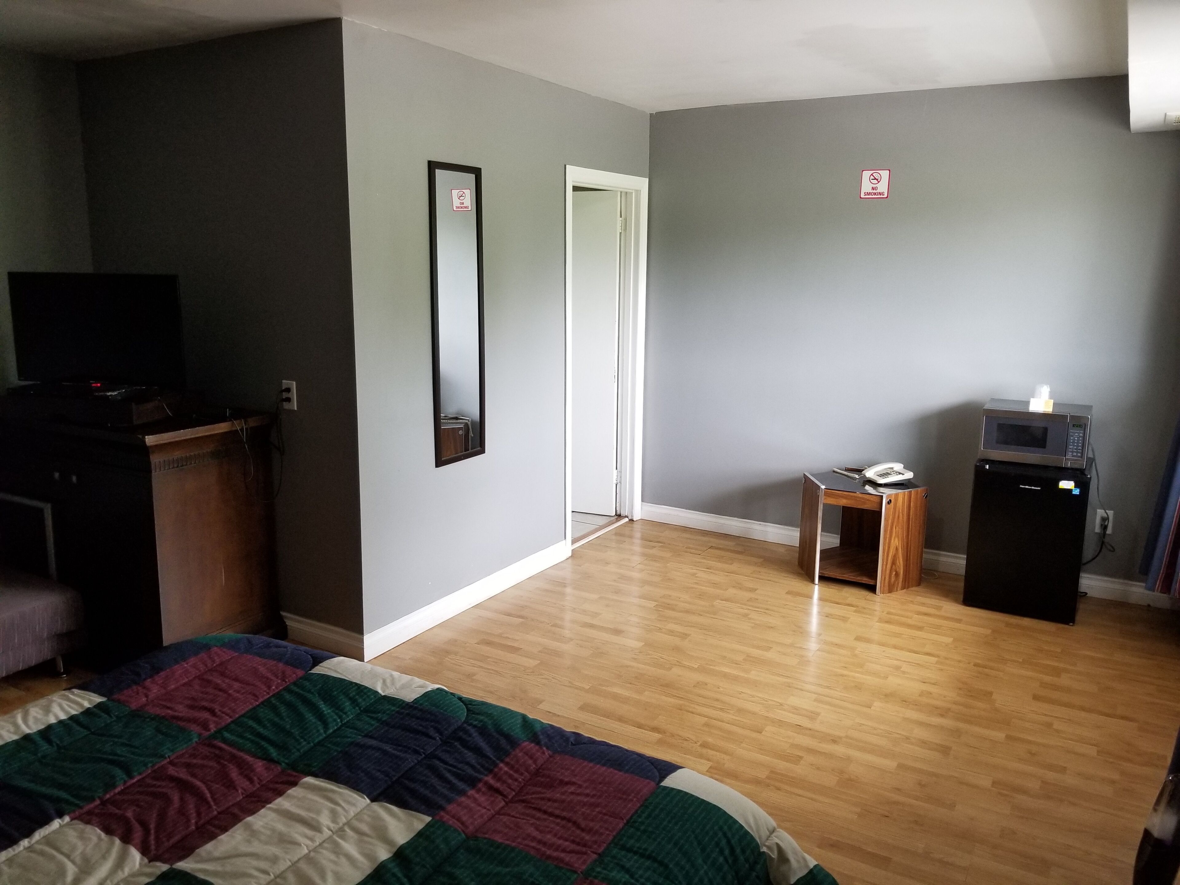Quarto com cama, penteadeira, televisão, micro-ondas e porta com placa de 'proibido fumar'.