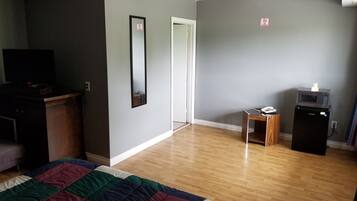 Quarto com cama, penteadeira, televisão, micro-ondas e porta com placa de 'proibido fumar'.