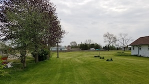 Ein gepflegter Rasen mit Baum, einer kleinen Werkstatt und einem Haus im Hintergrund.