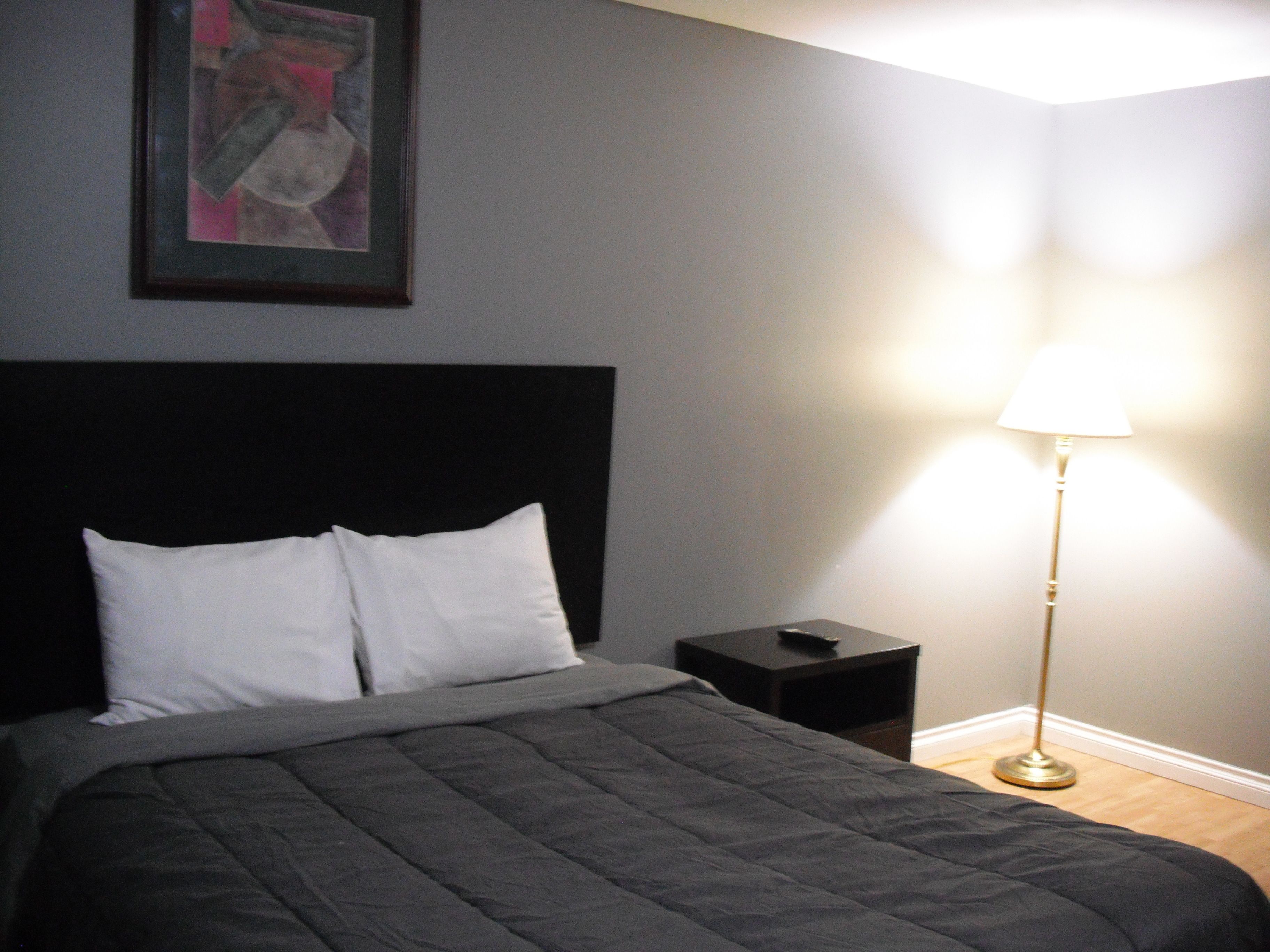 A neatly made bed with a black headboard and white pillows, a bedside table with a lamp, and a framed picture on the wall.