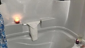 Eine Badewanne mit einem weißen Handtuch, einer brennenden Kerze und einem Glas Wasser.