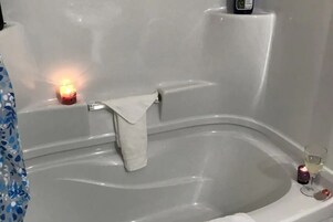 Una bañera con una toalla blanca, una vela encendida y un vaso de agua.
