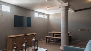 A spacious room with a large wooden cabinet, a flat-screen TV mounted on the wall, a wooden bench, and a large column. - Casa Brunella Hotel Boutique (Querétaro)