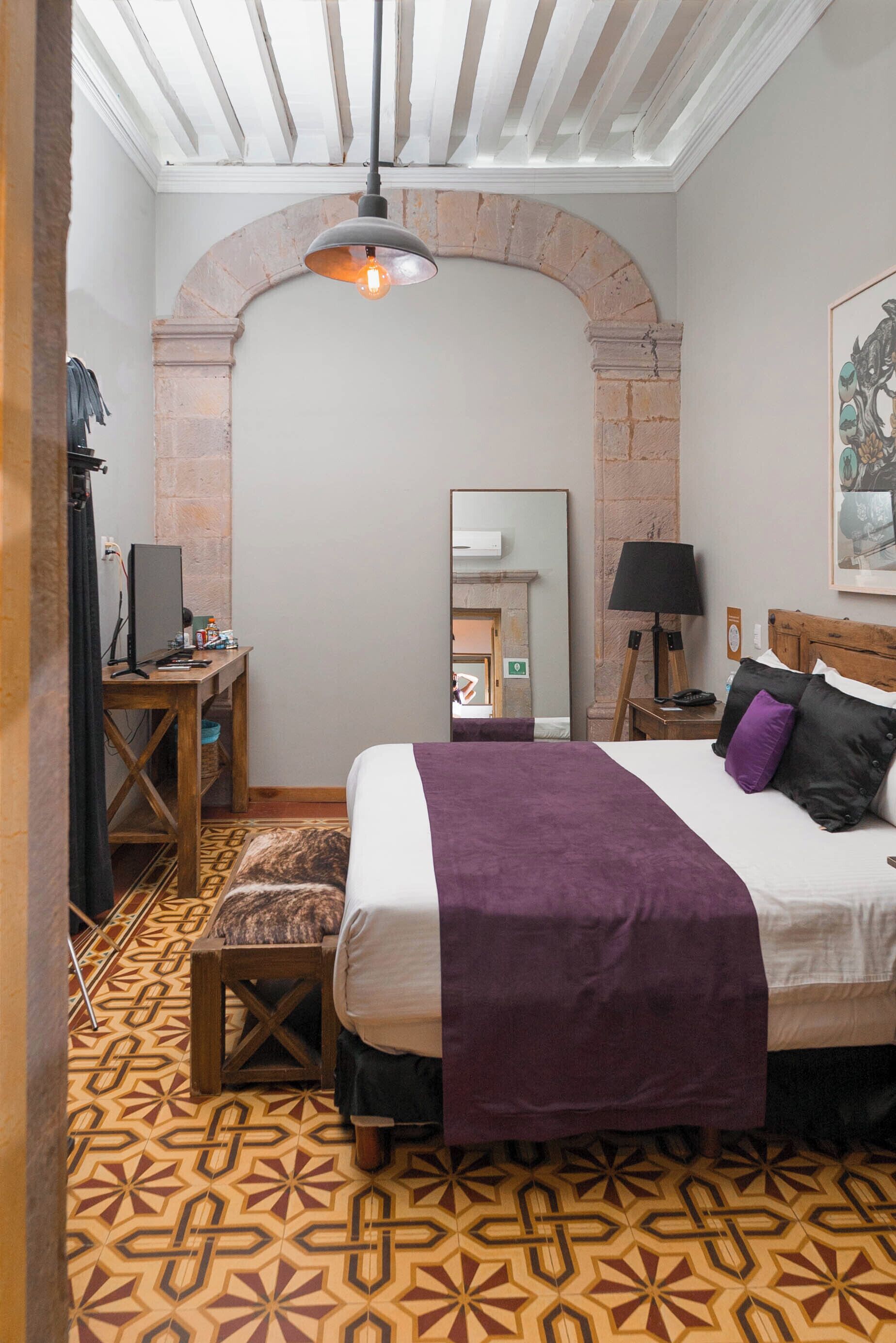 A bedroom with a bed, a desk, a lamp, and a mirror.