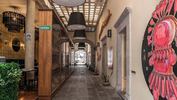 A hotel corridor with a wooden reception desk, a sign reading "ENTRADA," and a large decorative wall piece. - Casa Brunella Hotel Boutique (Querétaro)