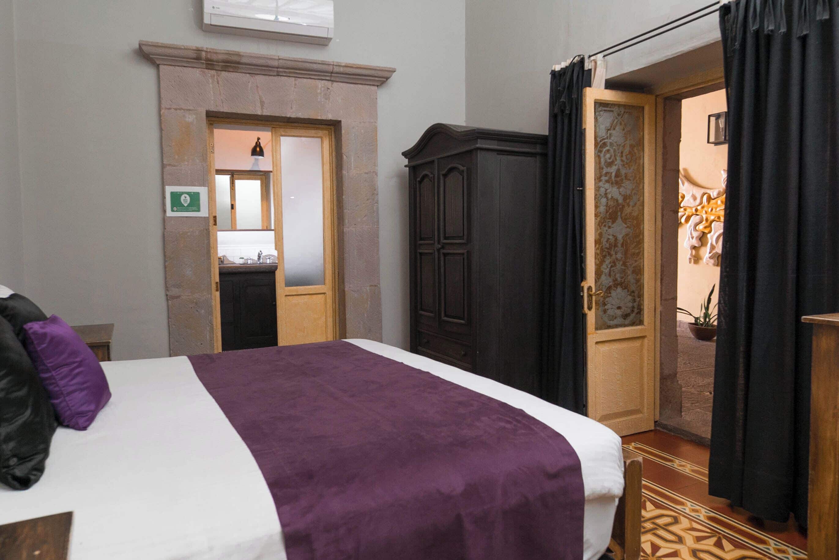 A hotel room with a bed, a wardrobe, and a door leading to a bathroom.