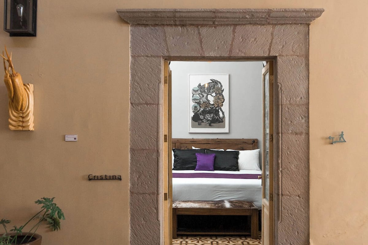 Una puerta que da a un dormitorio con una cama, una obra de arte enmarcada sobre la cama y una planta en maceta a la izquierda.