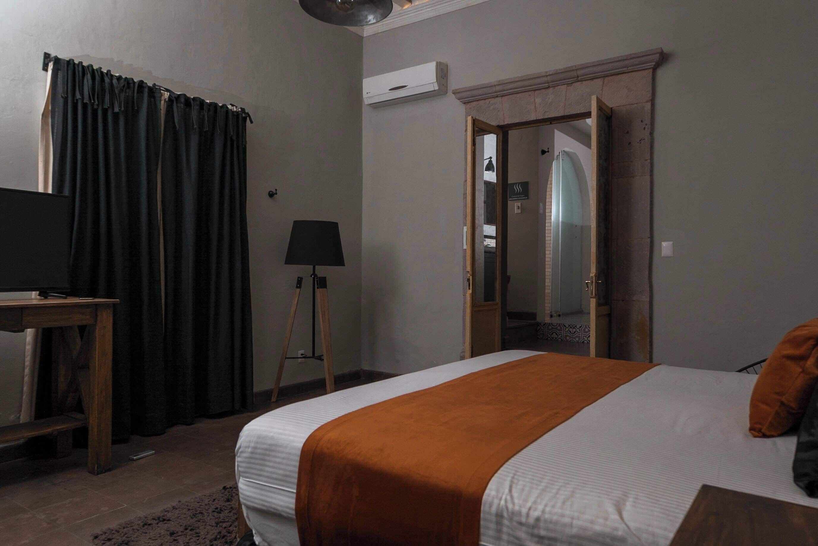 Um quarto com cama, escrivaninha, luminária e guarda-roupa.