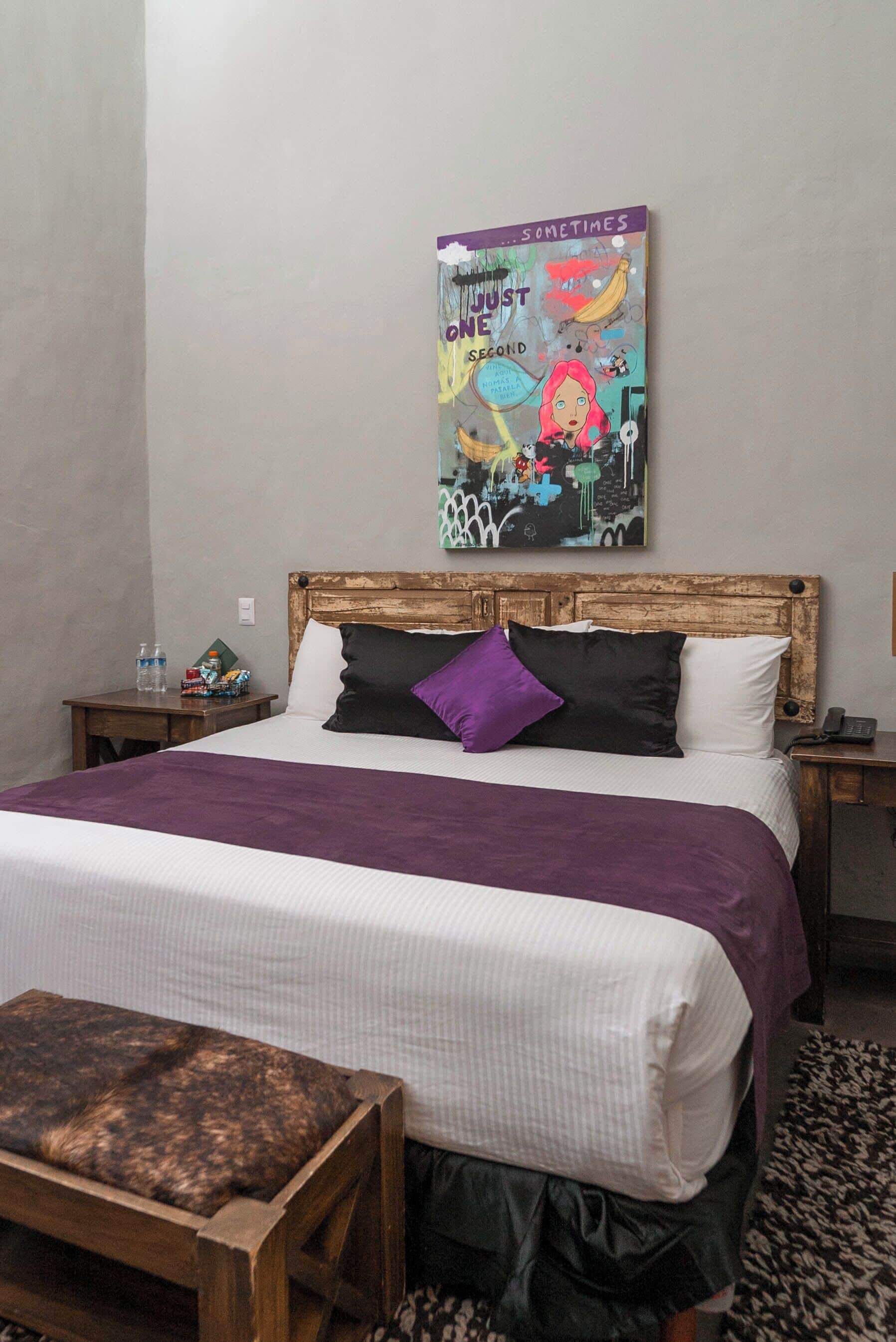 A neatly made bed with a purple blanket, a wooden headboard, and a colorful poster on the wall.