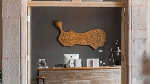 A reception area with a wooden reception desk, a computer, and a wall-mounted decorative piece. - Casa Brunella Hotel Boutique (Querétaro)