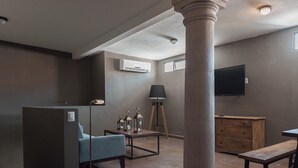A room with a large column, a blue sofa, a wooden table with lanterns, a wooden dresser, and a mounted TV. - Casa Brunella Hotel Boutique (Querétaro)
