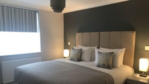 Ein ordentlich bezogenes Bett mit einer grauen Decke, einem dunklen Kopfteil und zwei Nachttischlampen.