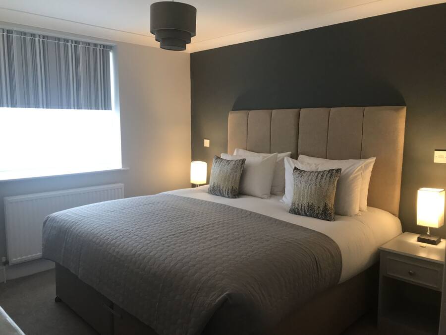 A neatly made bed with a grey quilt, a dark headboard, and two bedside lamps.
