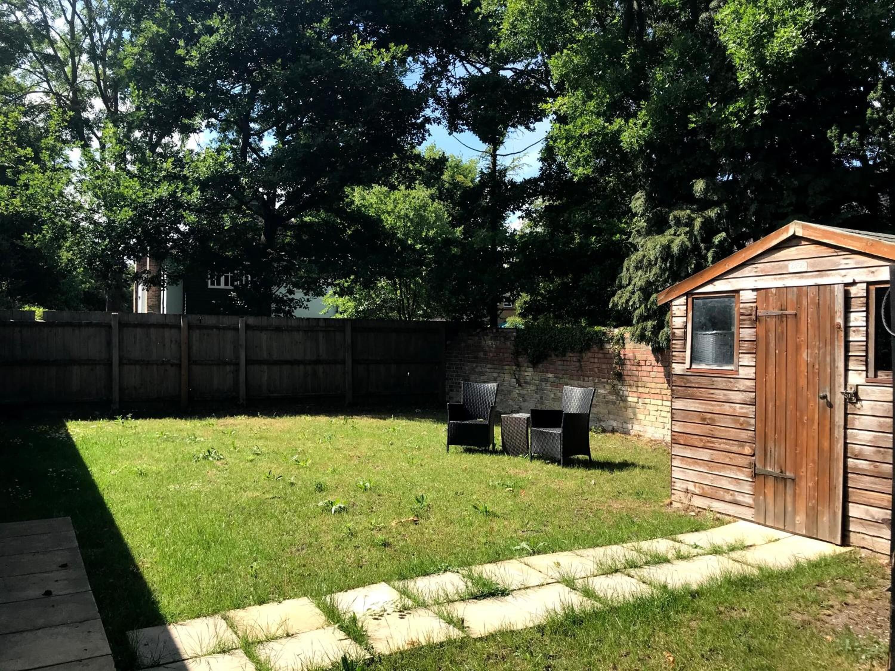 A backyard with a wooden shed, a barbecue grill, and a paved patio area.