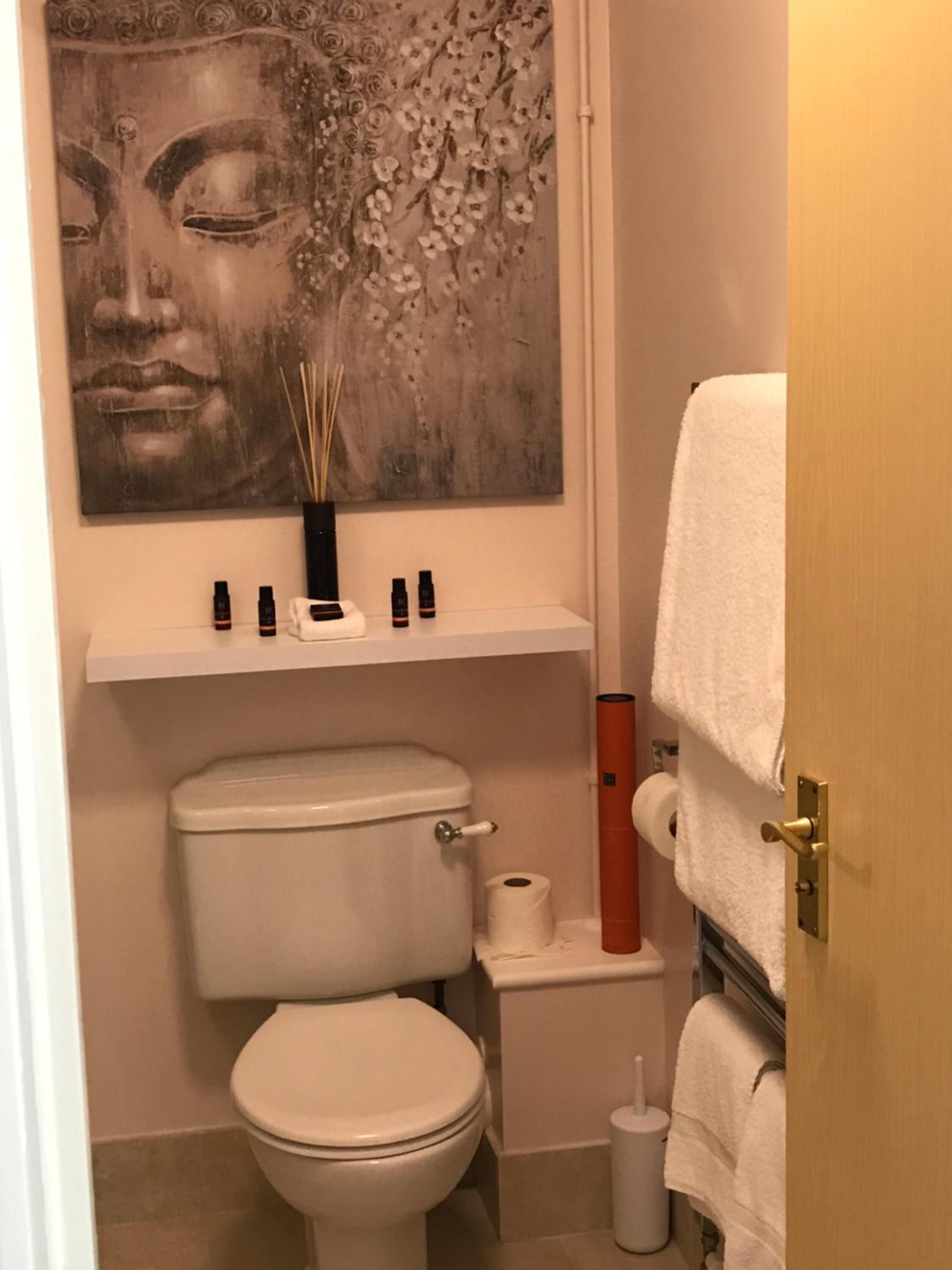 A bathroom with a toilet, a shelf with toiletries, a toilet paper holder, and a towel rack.