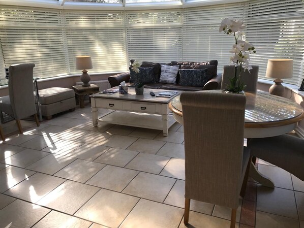 A sunlit room with a sofa, chairs, a coffee table, and a dining table. - The Old School House Rooms (Cambridge)