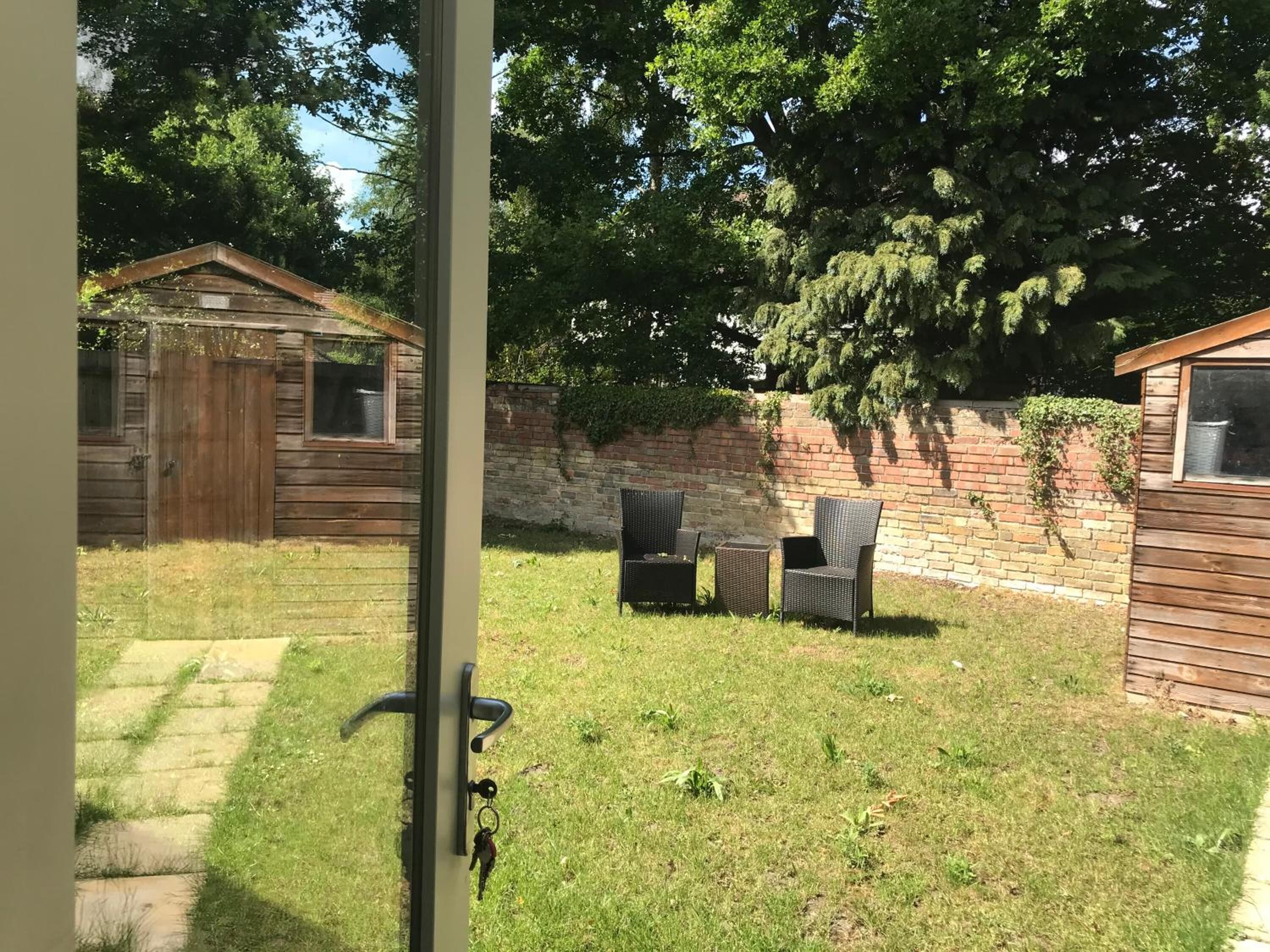 Ein Garten mit Holzschuppen, einer Ziegelmauer und einer Terrasse mit Stühlen und Tisch.