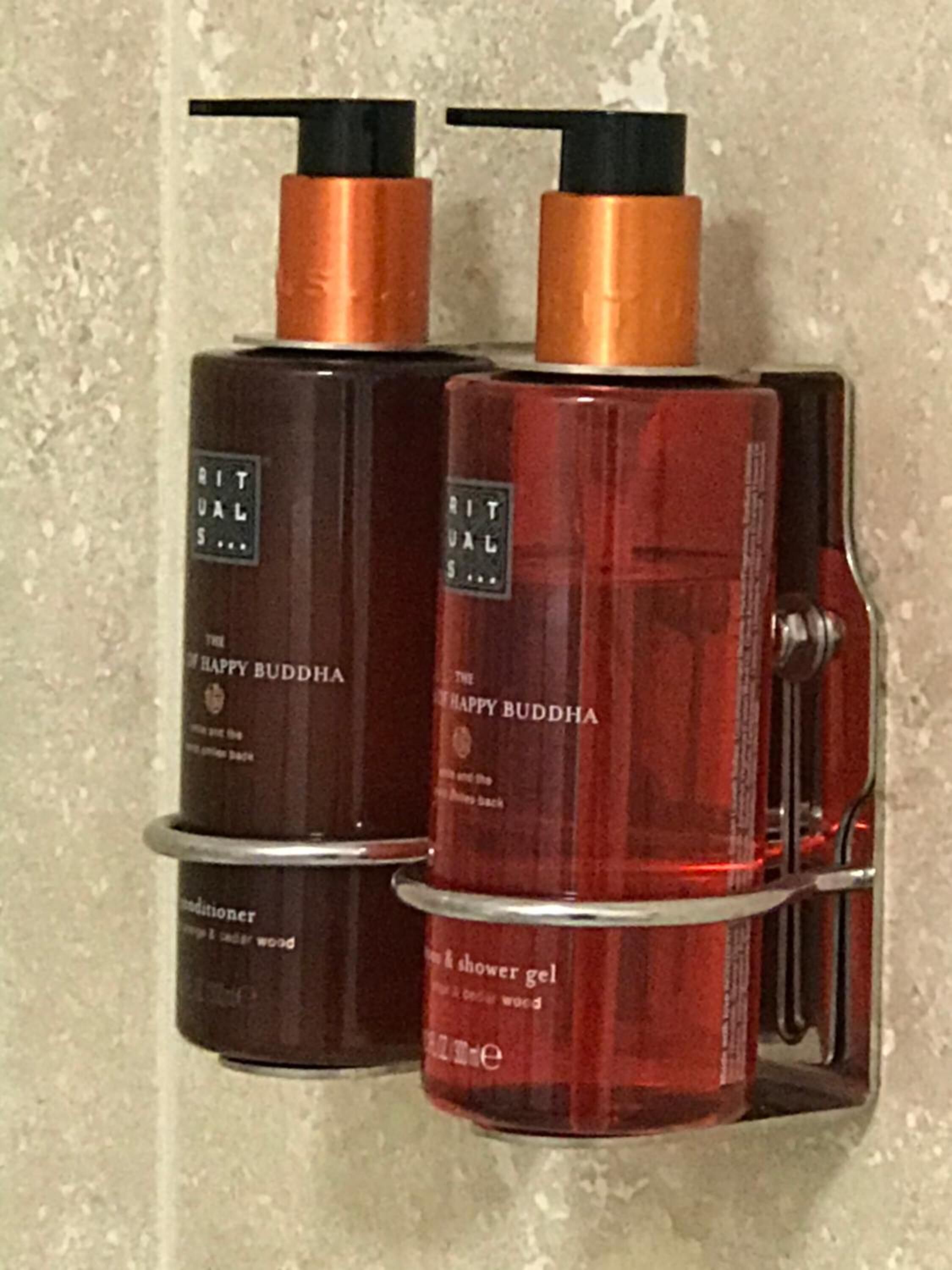 Two bottles of The Happy Buddha shower gel on a shelf.
