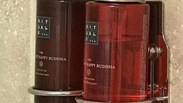 Two bottles of The Happy Buddha shower gel on a shelf.