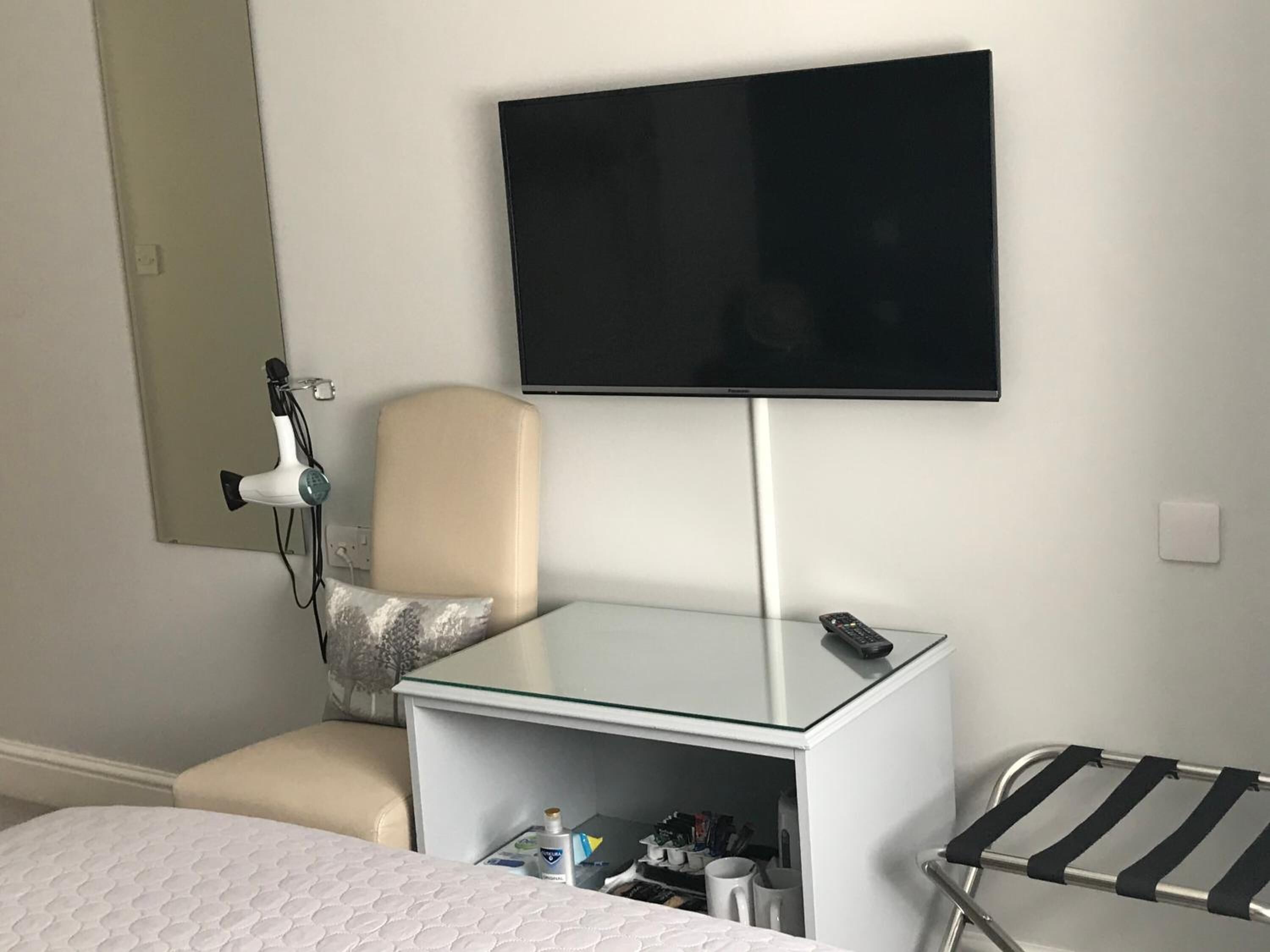 A hotel room with a bed, a chair, a TV mounted on the wall, a small table, and a drying rack.