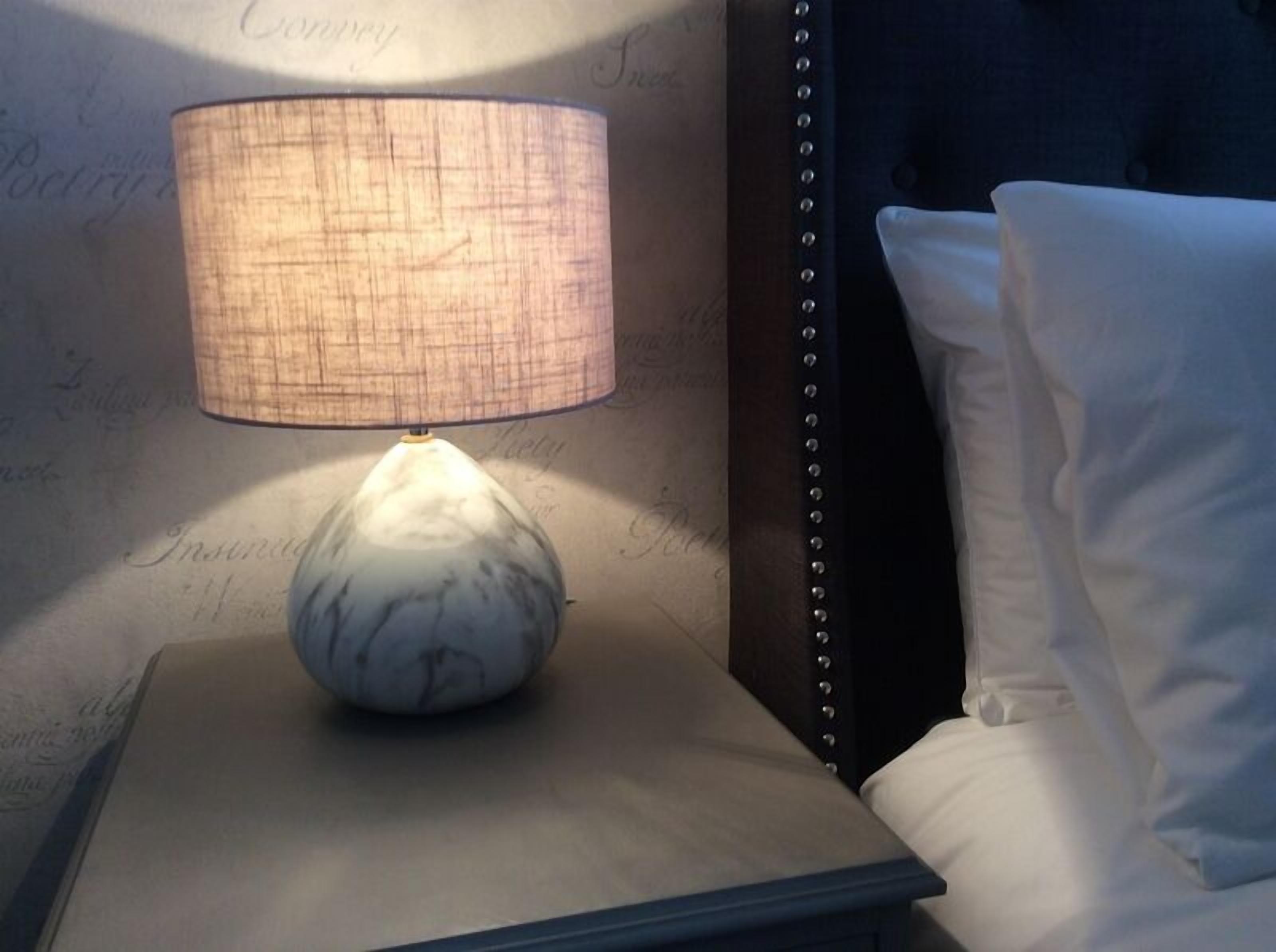 A bedside table with a lamp, a pillow, and a headboard.