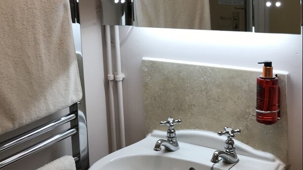 Ein Badezimmer mit Waschbecken, zwei beleuchteten Spiegeln und einem Handtuchhalter.