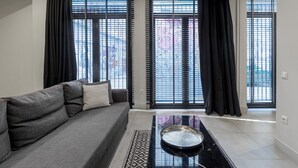 Un salon moderne avec un canapé gris, des rideaux noirs et un sol carrelé.