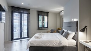 Une chambre à coucher moderne avec un grand lit, un bureau avec une lampe et une vue à travers les stores de la fenêtre.