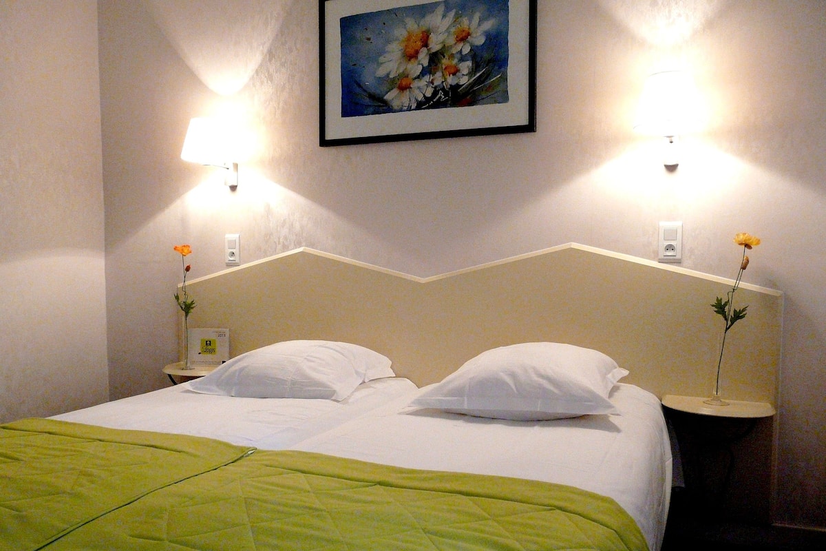 Ein Hotelzimmer mit einem Bett, zwei Nachttischen, einer grünen Bettdecke und zwei Wandlampen.