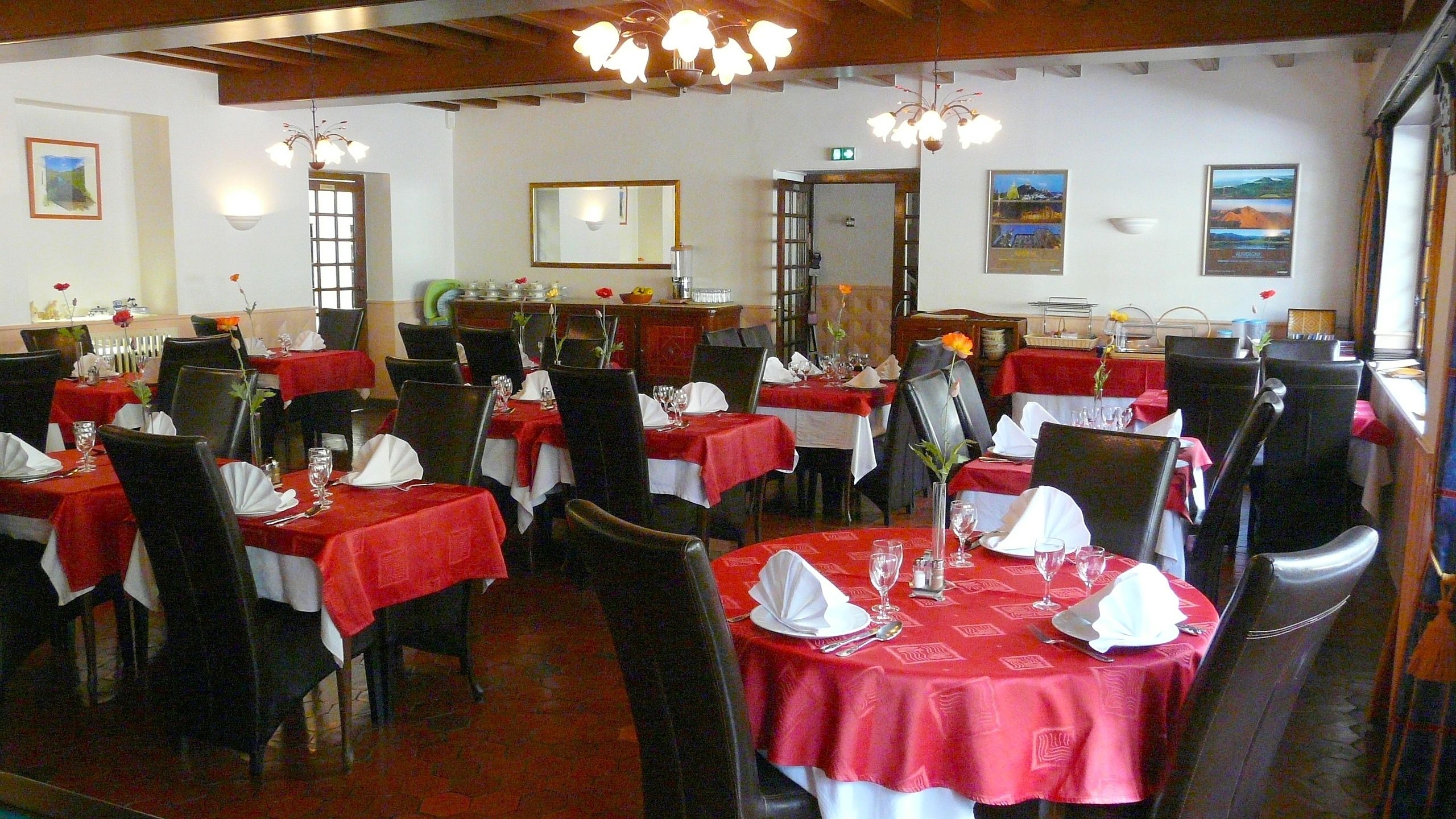 A restaurant with multiple tables set for dining, featuring red tablecloths and black chairs.