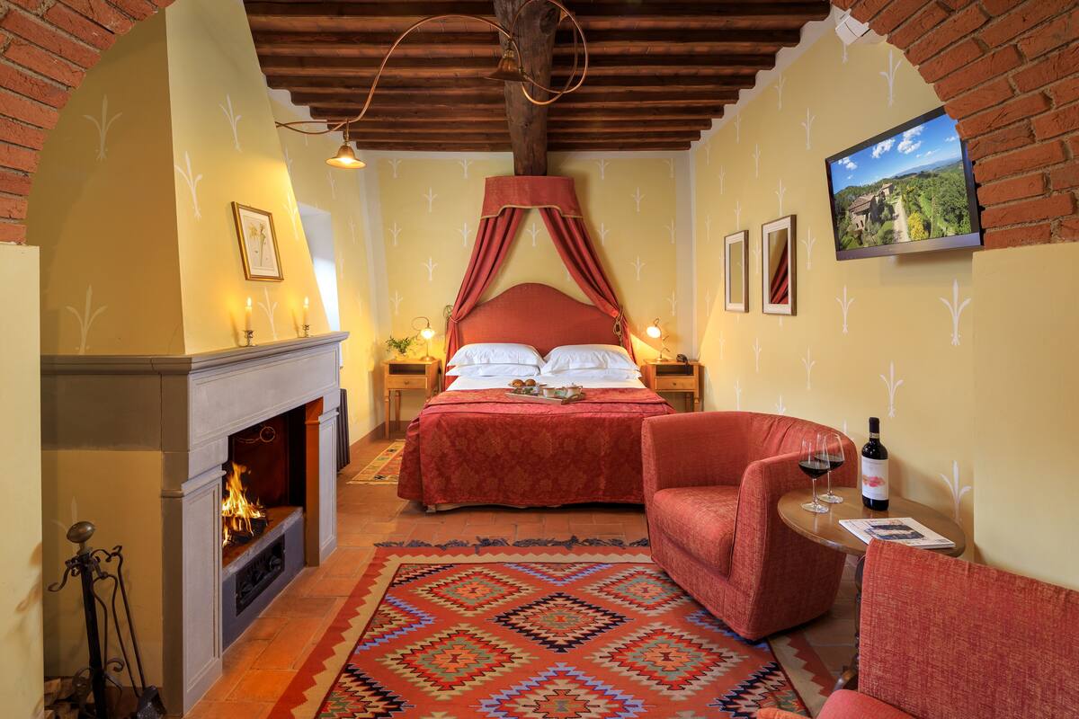 Un dormitorio con chimenea, una cama con dosel, un televisor en la pared y una mesita con una botella y vasos.