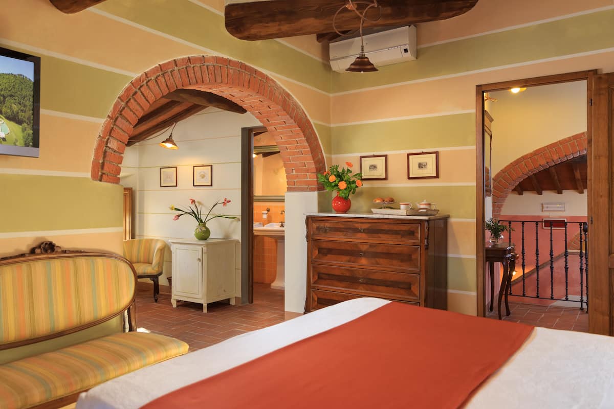 Una habitación de hotel con una cama, un sillón a rayas, un aparador de madera y un arco de ladrillo.
