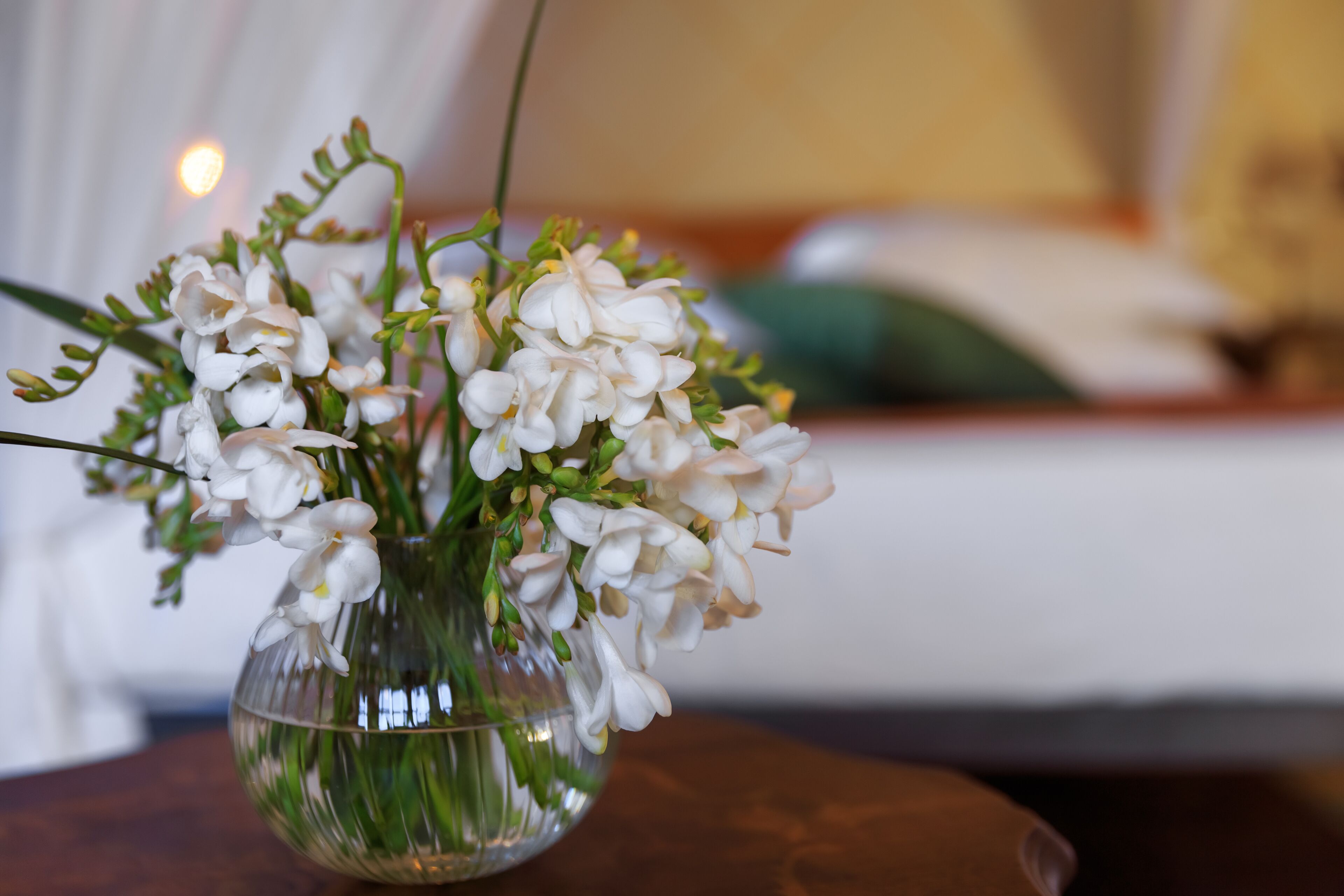A clear glass vase with white flowers on a wooden surface.