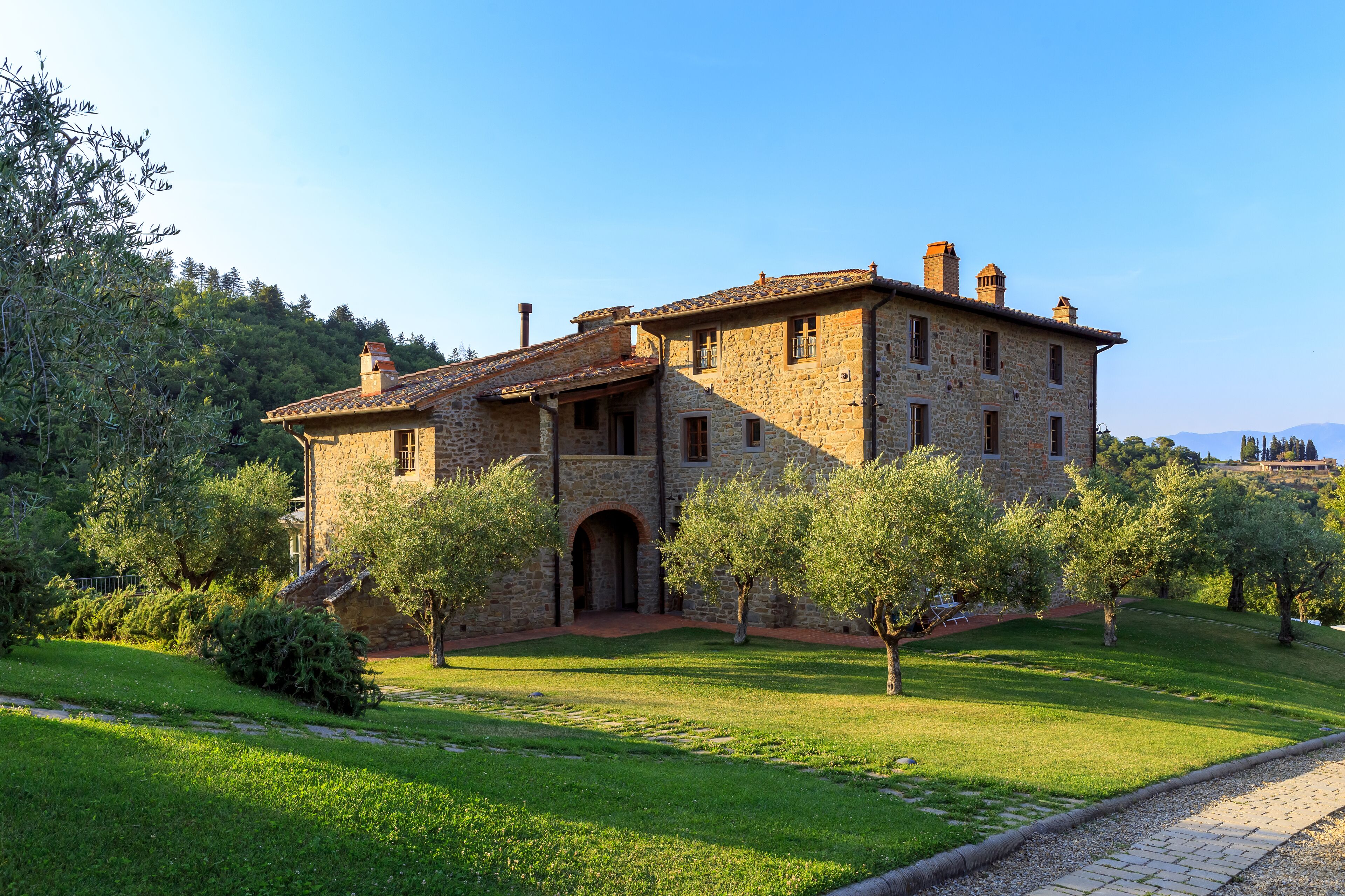 A stone building with a courtyard, surrounded by trees and a clear sky.