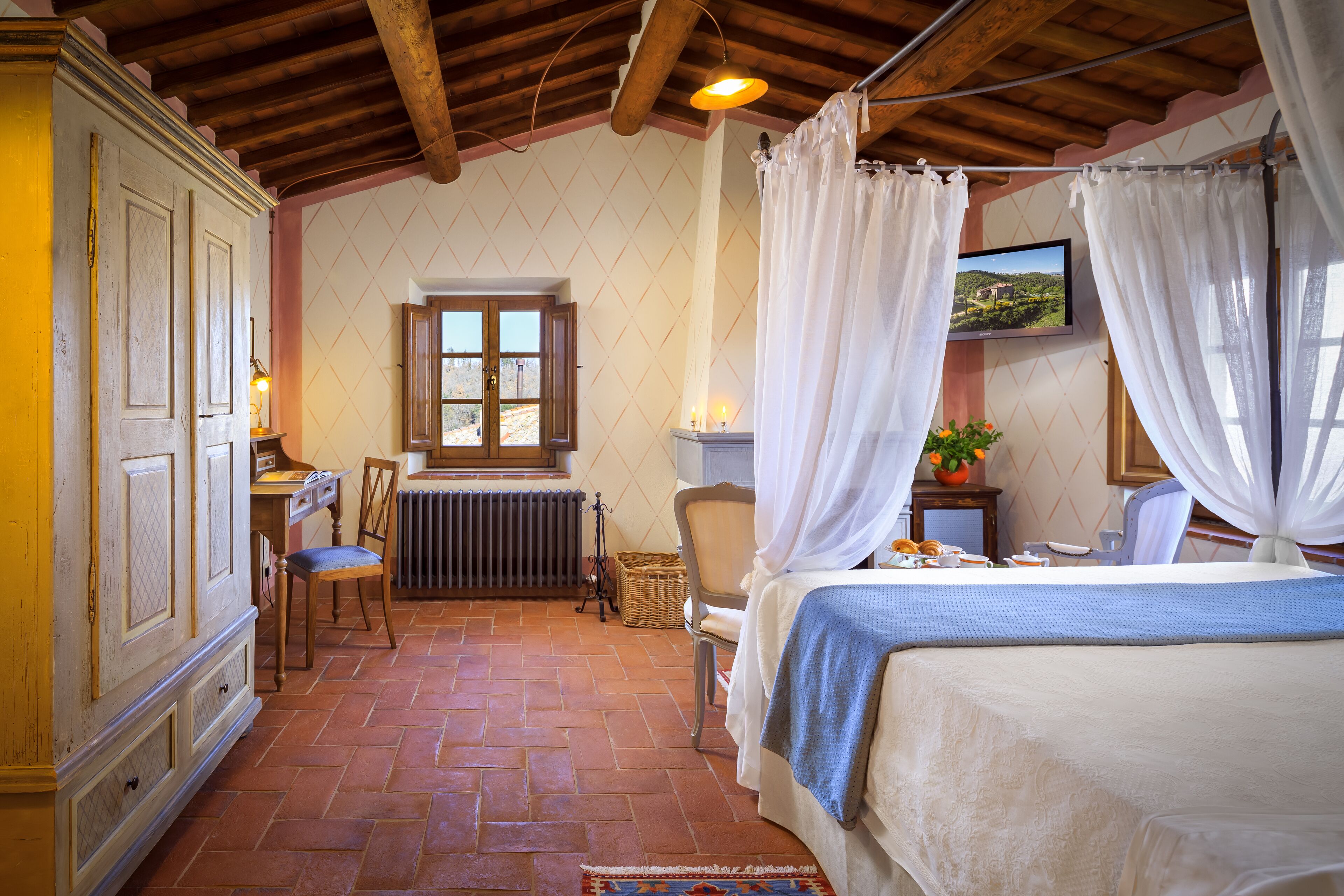 A bedroom with a bed, a chair, a table with a plant, and a window with curtains.