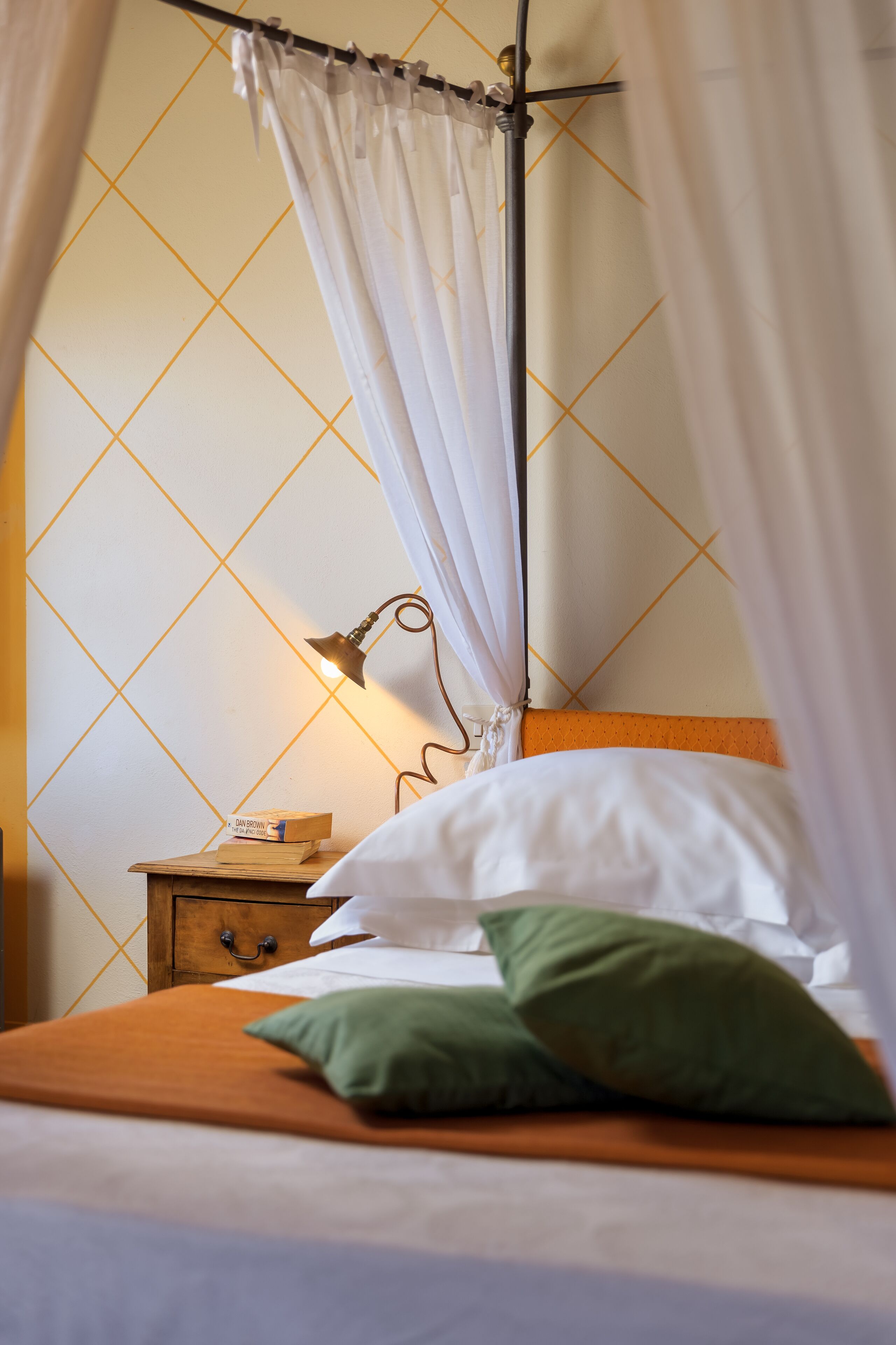 A neatly made bed with white linens, a green pillow, and a wooden nightstand with a lamp.