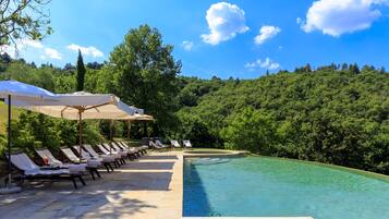 Un espace aménagé au bord de la piscine, avec des chaises longues et des parasols, entouré d’une végétation luxuriante et surplombé d’un ciel bleu azur.