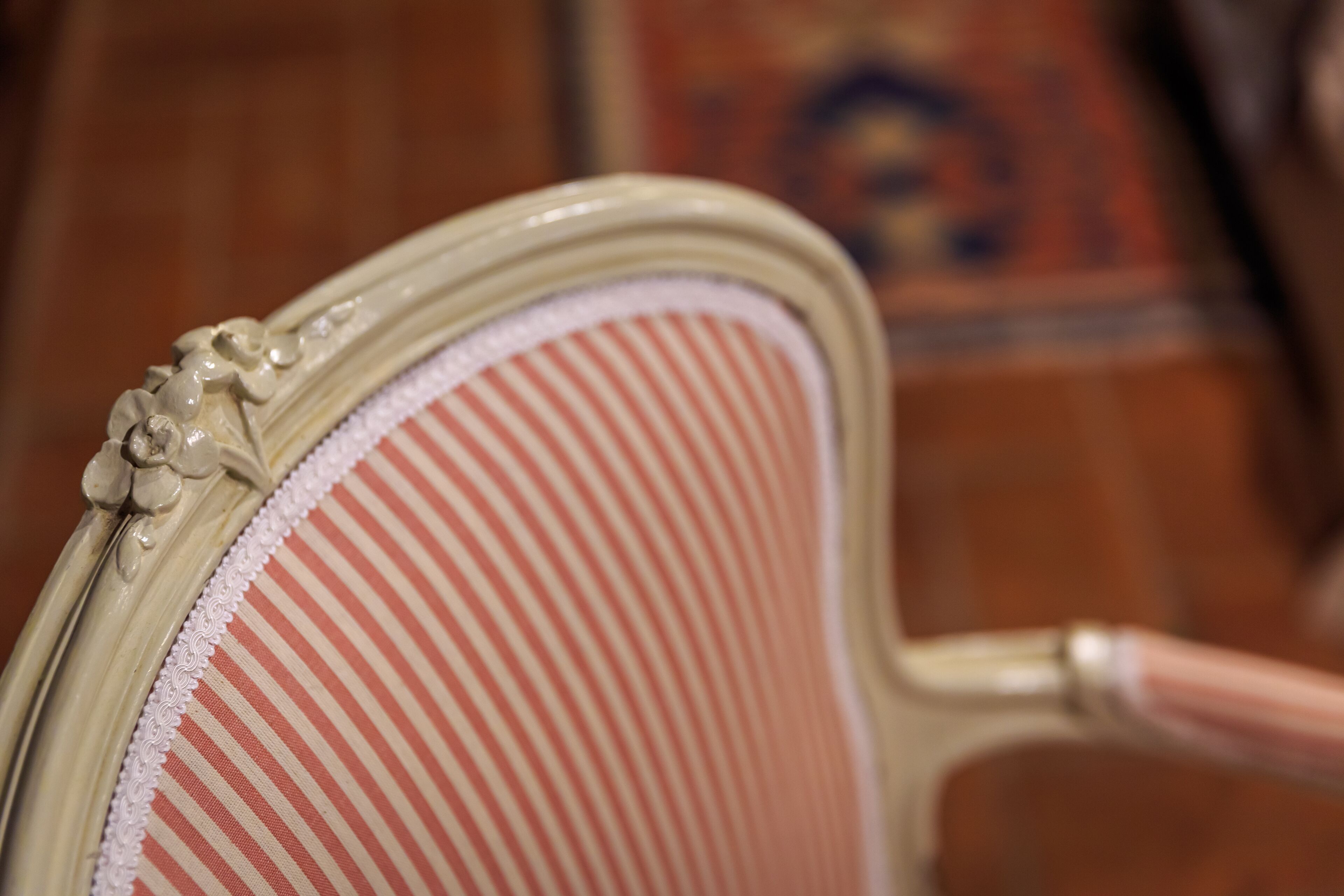 A close-up of a chair with a striped fabric and a decorative floral pattern on the backrest.