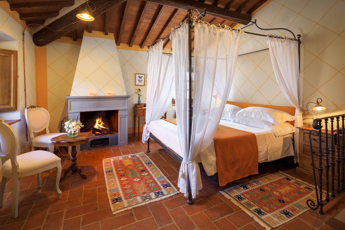 Un dormitorio con cama de dos columnas, chimenea y suelo de baldosas rústicas.