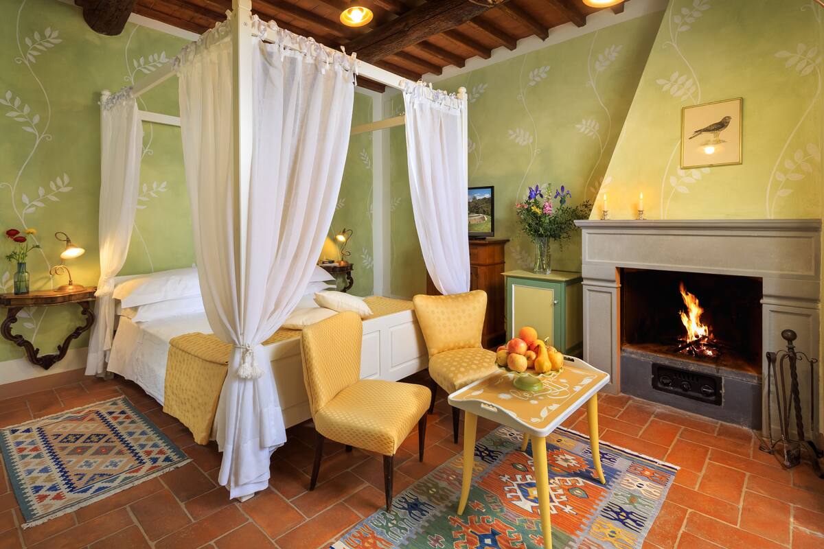 Un dormitorio con cama con dosel, chimenea y mesa de comedor con fruta.