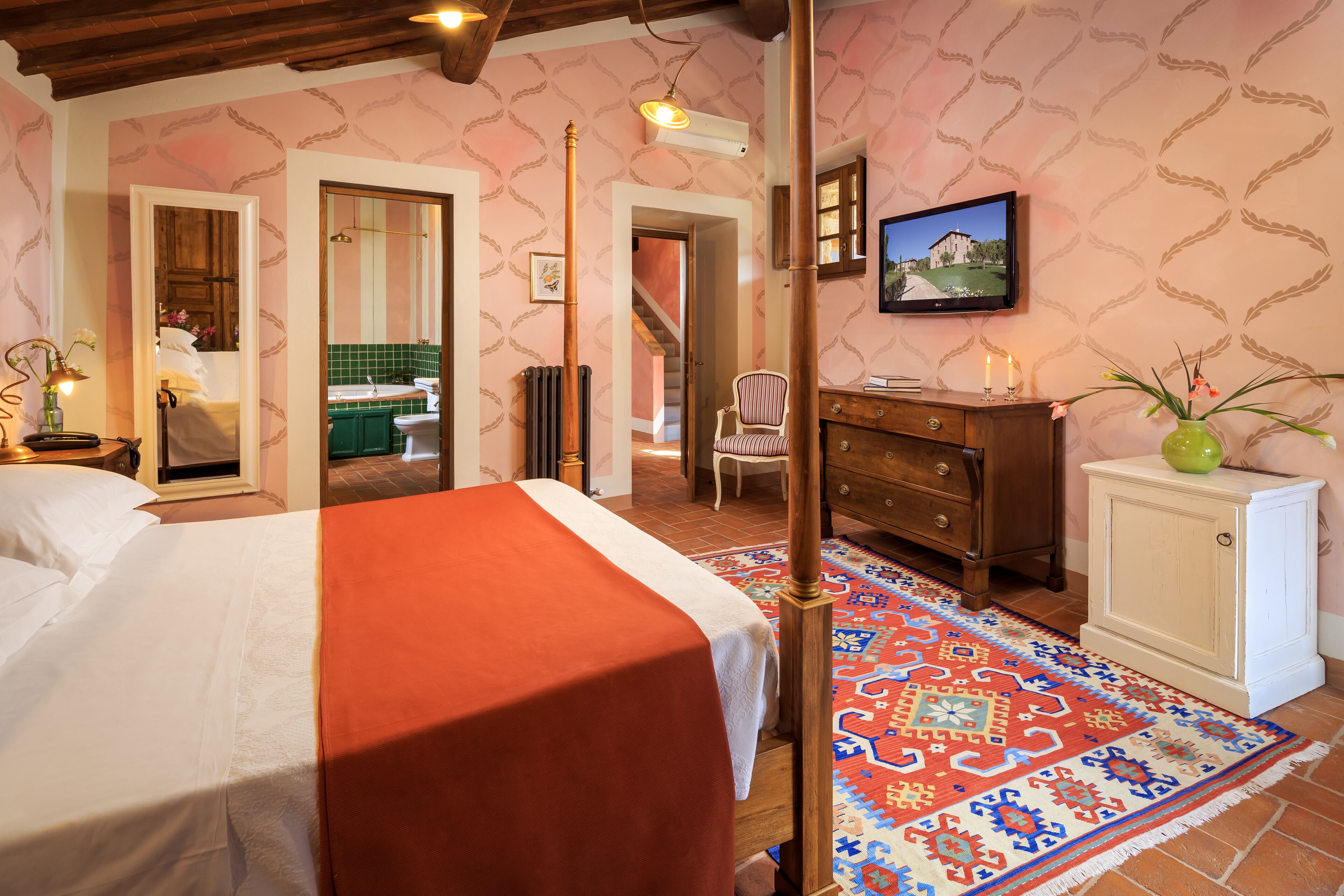 Quarto com cama, penteadeira, espelho, televisão e tapete estampado.